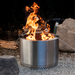 Stainless steel fire pit with flames burning, surrounded by rocks and wood.