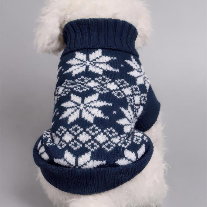 A white fluffy dog wearing a navy blue knit sweater with a white snowflake and diamond pattern, shown from behind against a neutral gray background.