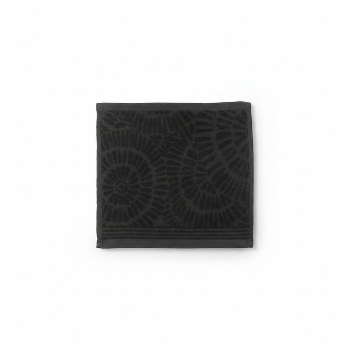 A dark charcoal gray square towel featuring a tonal embossed spiral and leaf-like pattern, shown flat against a plain white background.