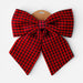 A large fabric bow in a red and black buffalo plaid pattern, attached to a brown cardboard hanger against a light gray background.
