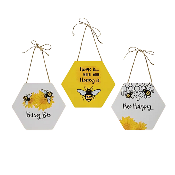 Assorted bee-themed hexagon signs with sayings — Busy Bee, Bee Happy, and Home is… Where Your Honey Is — featuring yellow, white, and honeycomb designs with jute hangers.