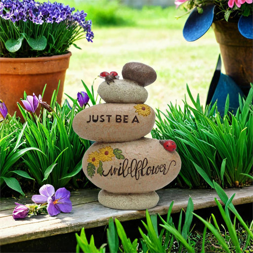 Decorative stone stack with 'Just Be A Wildflower' text in a garden setting