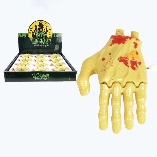 Halloween wind-up toy hand candy shown next to its retail display box. The hand is flesh-toned with red blood splatter details, and the box features a black background with a yellow moon graphic and 'Happy Halloween Wind-Up Toy' text.