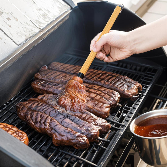 Person grilling steaks on a barbecue with a brush applying sauce.