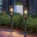 Two solar garden lights on stakes in a garden setting with a brick path.