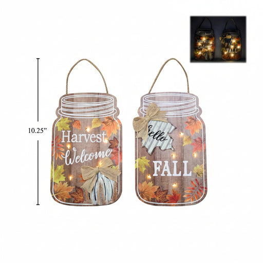 Two fall-themed mason jar wall hanging signs with rope loops, shown on a white background. One sign reads “Harvest Welcome” and the other reads “Hello FALL,” both decorated with autumn leaves, a bow, and warm string lights.