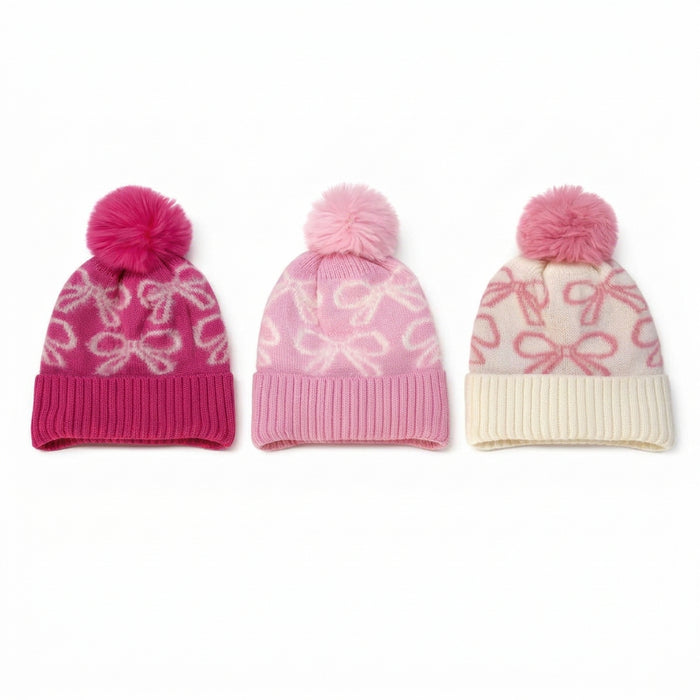 Three pink knit pom-pom beanies with bow patterns, displayed side-by-side on a white background.