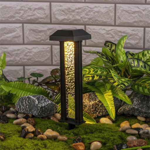 Garden light fixture with decorative stones and plants against a brick wall.