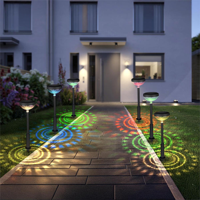 Solar-powered garden lights casting colorful patterns on a pathway in front of a house.