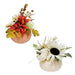 Two artificial autumn floral pumpkin arrangements on a plain white background. One arrangement features red, orange, yellow, and white flowers in a peach-colored pumpkin base, and the other features white and cream flowers with a dark brown sunflower center in an off-white pumpkin base.