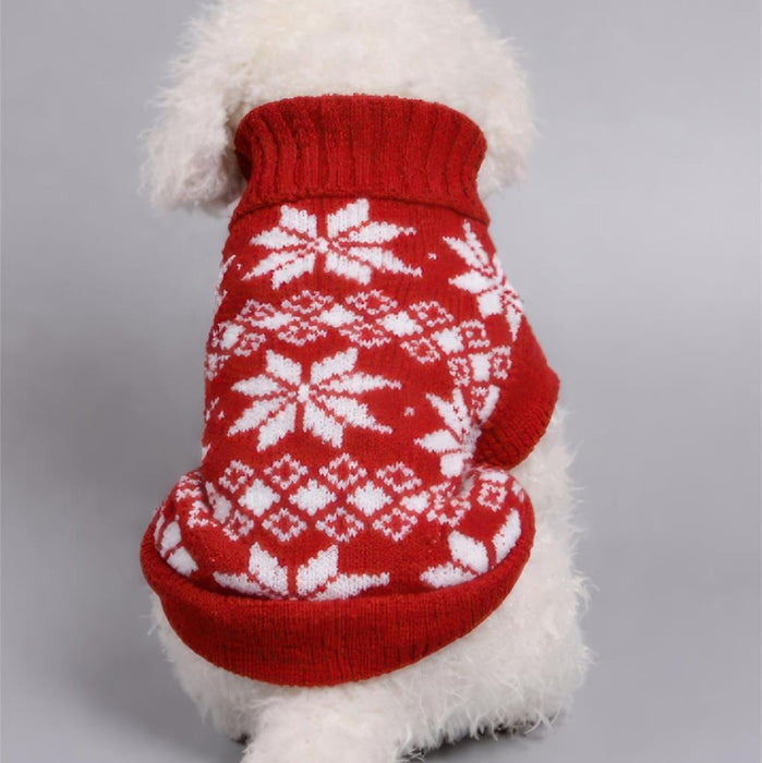 A small white dog wearing a red knit sweater with a white snowflake and diamond pattern, photographed against a plain light gray background.