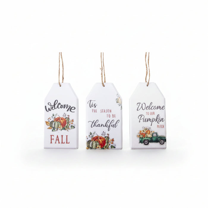 Three white hanging decorative tags with autumn-themed printed designs on a white background. The left tag says 'Welcome FALL' with pumpkins and fall leaves.