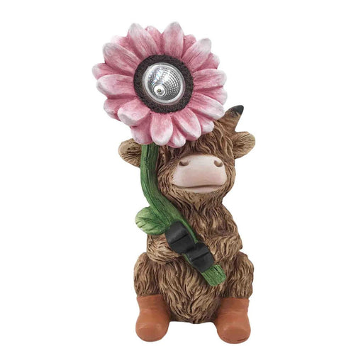 Small figurine of a cow with a pink flower on its head and a green leaf around its neck, set against a white background.
