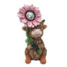 Small figurine of a cow with a pink flower on its head and a green leaf around its neck, set against a white background.