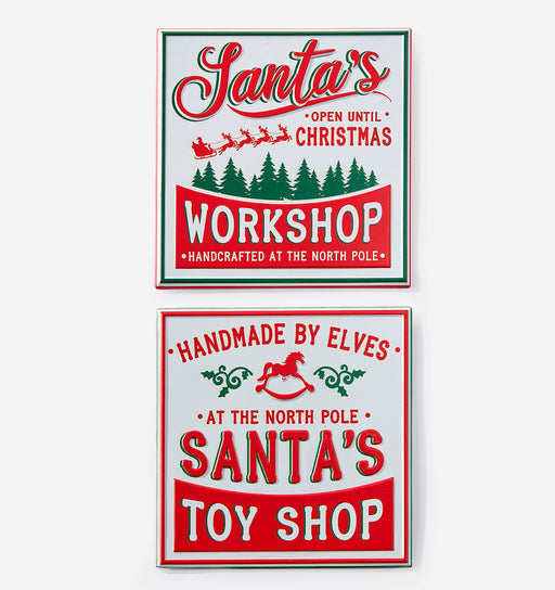 Two vintage-style Christmas sign designs shown on a light gray background. The top sign reads 'Santa's Workshop' with red lettering, green border accents, and green pine trees.