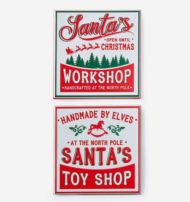 Two vintage-style Christmas sign designs shown on a light gray background. The top sign reads 'Santa's Workshop' with red lettering, green border accents, and green pine trees.