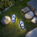 Two flip-flop-shaped solar lights on grass with rocks in the background