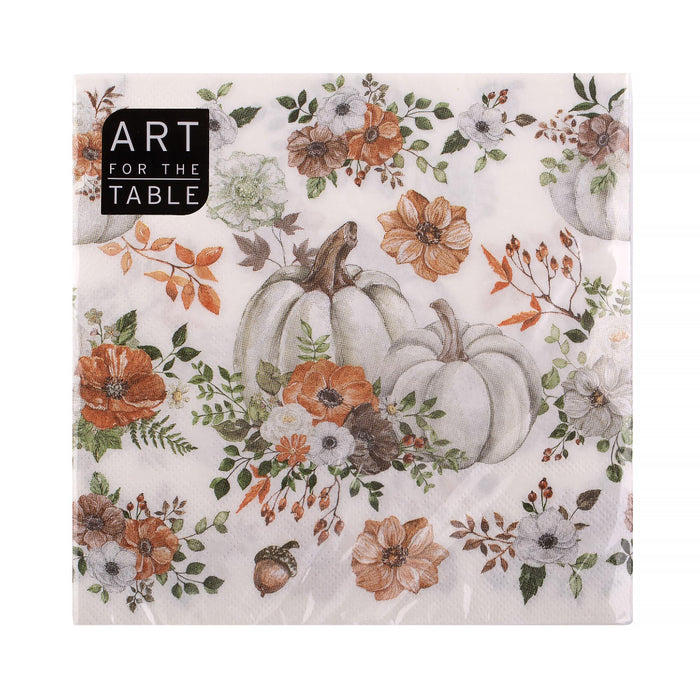 A square paper napkin with a fall harvest floral print, featuring watercolor-style pumpkins, orange and white flowers, and green leaves on a cream background. A black label in the top-left corner reads 'ART FOR THE TABLE'.