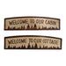 Two wooden signs with 'Welcome to our cabin' and 'Welcome to our cottage' text on a white background.