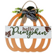 A decorative autumn hanging sign shaped like a pumpkin, with a white front panel reading “hello Pumpkin” in brown and green lettering, plus leaf illustrations. The sign has an orange scalloped pumpkin frame, a rope hanger, a burlap ribbon bow, and greenery accents on a white background.