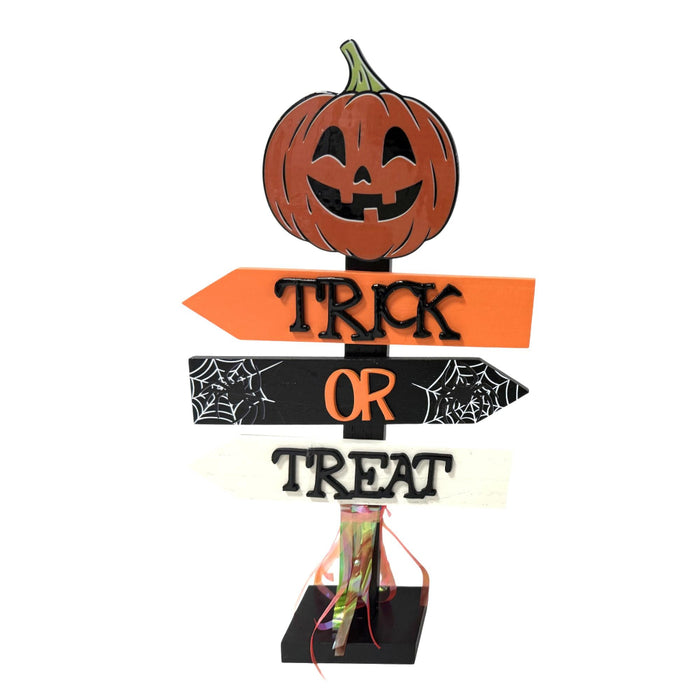 Halloween decorative signpost with a carved pumpkin at the top and three directional arrows reading “TRICK OR TREAT” on a white background.
