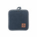 A square dark blue denim pot holder with a gray fabric trim and handle, featuring a brown leather patch with a clover design in the bottom right corner, set against a plain white background.