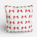 A square white textured throw pillow featuring a repeating pattern of red glittery bows, shown against a light gray studio background.