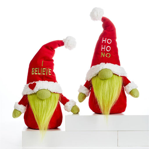 Two festive Christmas gnome plush toys standing on white display blocks against a white studio background. One gnome wears a red Santa-style hat with white trim and says "I BELIEVE" in gold lettering, while the other wears a matching hat with "HO HO NO" in gold lettering.