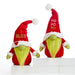 Two festive Christmas gnome plush toys standing on white display blocks against a white studio background. One gnome wears a red Santa-style hat with white trim and says "I BELIEVE" in gold lettering, while the other wears a matching hat with "HO HO NO" in gold lettering.