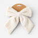 A fluffy cream-colored bow accessory attached to a brown cardboard hanger, shown against a light gray background.