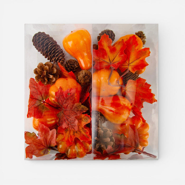 A square clear acrylic or glass decorative tray or block containing an autumn arrangement of faux pumpkins, red and orange maple leaves, and brown pinecones, photographed against a plain white background.