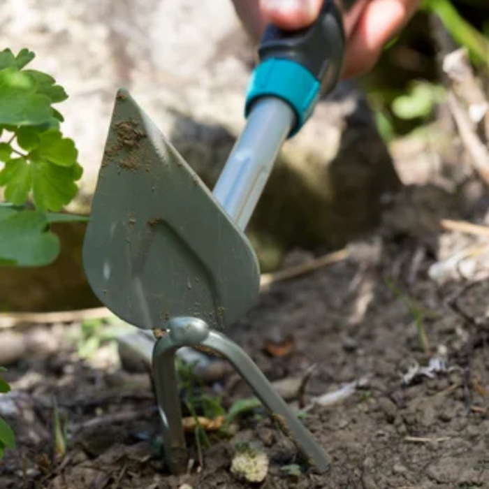 Gardening tool being used in a garden setting with soil and plants visible.