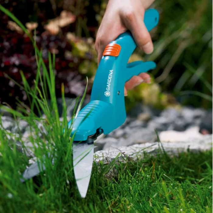 Person using a garden tool to cut grass near a stone path