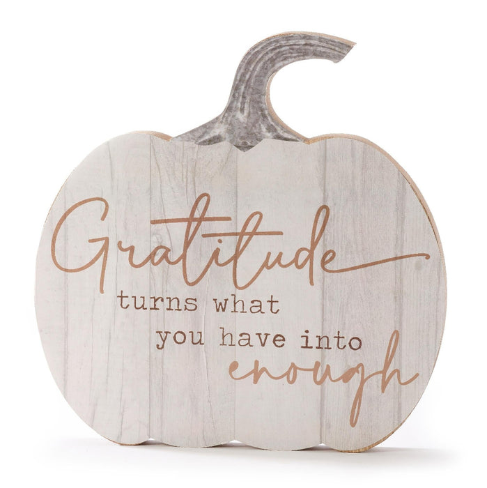 A pumpkin-shaped decorative sign with a whitewashed wood finish and a gray faux-stem top. The sign features the engraved quote, 'Gratitude turns what you have into enough' in a warm brown script and serif font, set against a plain white background.