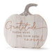 A pumpkin-shaped decorative sign with a whitewashed wood finish and a gray faux-stem top. The sign features the engraved quote, 'Gratitude turns what you have into enough' in a warm brown script and serif font, set against a plain white background.