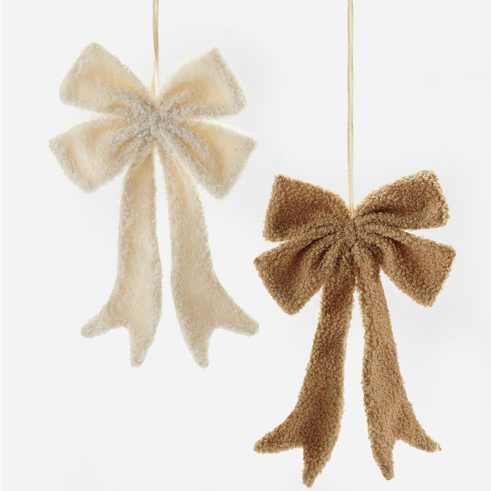 Two fuzzy fabric bow ornaments hanging against a plain white background, one in cream and one in tan.