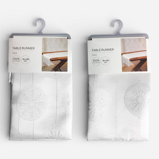 Two packaged table runners hanging on gray plastic hangers against a light gray background. Each package contains a folded white table runner with a subtle snowflake pattern and a printed header card labeled 'TABLE RUNNER' with 'STACK' and size details.