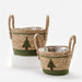 Two woven seagrass baskets with rope handles, decorated with green tree motifs and green bands, shown on a clean white studio background.