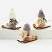 Three small decorative gnome figures wearing knit winter hats and long yarn beards, each mounted on a wooden sled with skis, photographed on a clean white studio background.